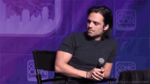 a man is sitting at a table with a microphone in front of a wall that says salt lake comic con .