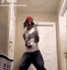 a man in a red hat and white shirt is dancing in a hallway .