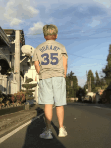 a person wearing a durant 35 t-shirt stands on a street