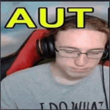 a man wearing headphones and glasses is sitting in a chair with the word aut on his face .