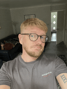 a man wearing glasses and a mckenzie t-shirt takes a selfie