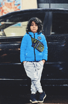 a young boy wearing a blue jacket and nike sweatpants leans against a black car