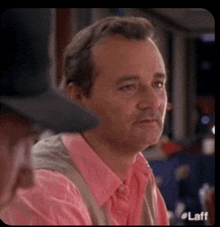 a man in a pink shirt is sitting at a table with other people