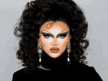 a drag queen with a wig and earrings is wearing a black turtleneck and looking at the camera .