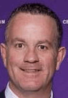 a man in a suit and tie is smiling for the camera on a purple background .