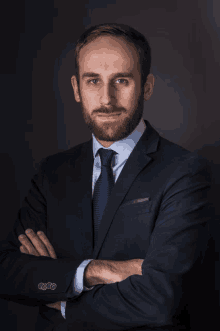 a man in a suit and tie with his arms crossed looks at the camera