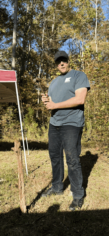 a man with a k on his shirt is holding a hammer in a field