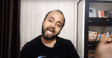 a man with a beard is making a funny face in front of a book shelf