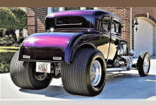 a black and purple hot rod is parked in front of a garage .