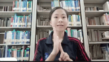 a woman wearing a black and red shirt with a blue emblem on it stands in front of a library filled with books