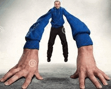 a man in a blue hoodie is being held by a pair of very large hands .