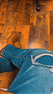 a person laying on a wooden floor wearing ripped jeans and boots