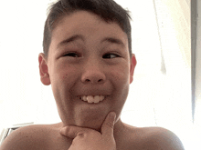 a young boy without a shirt is making a funny face with his hand on his chin