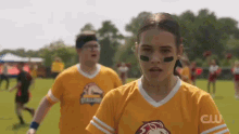 a woman wearing a yellow jersey with a lion on it is standing on a field with other people .