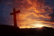 a cross is silhouetted against a sunset sky with birds flying around it