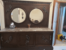 a wooden dresser with two mirrors and a vase on top