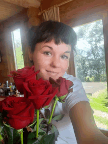 a woman holding a bunch of red roses in front of a window