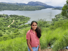 a woman in a pink shirt stands on a hill overlooking a lake