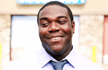 a man wearing a tie and a white shirt smiles in front of a sign that says ' ice cream '