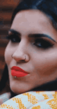 a woman with red lipstick and a nose ring is looking at the camera .