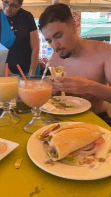 a shirtless man is eating a sandwich and drinking a smoothie