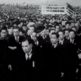 a black and white photo of a large group of men in suits and ties walking in a line .