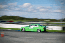 a green car is driving on a race track and has a sticker on the side that says enthusiast