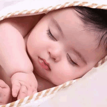 a baby is sleeping under a blanket on a bed .