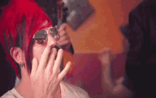 a woman with red hair and sunglasses is covering her mouth