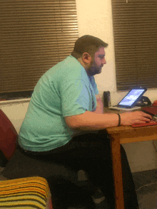 a man sits at a table with a laptop and a can of soda