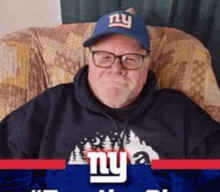 a man is sitting in a chair wearing a ny giants hat .