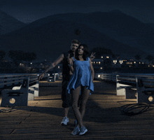 a man and a woman standing on a pier with mountains in the background