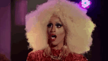 a drag queen with a large blonde afro is wearing a red dress .