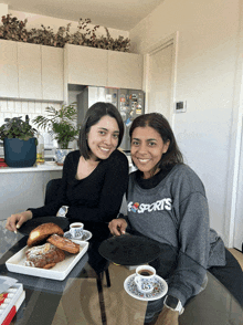 two women sitting at a table with a woman wearing a sports sweatshirt