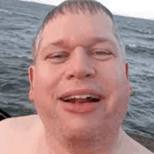 a shirtless man is standing in front of the ocean and smiling .