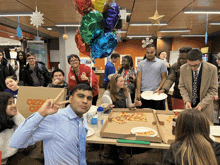 a group of people are gathered around a table with pizza and a cardboard box that says ozzy pizza on it