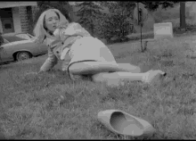 a black and white photo of a woman laying on the grass with a pair of shoes next to her .