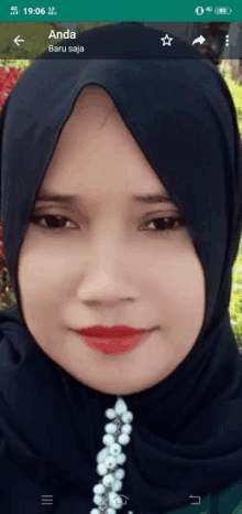 a woman wearing a black hijab and red lipstick is displayed on a phone screen