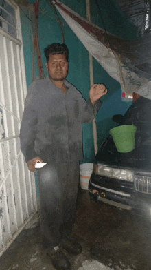 a man in overalls stands in front of a car with a green bucket on the hood