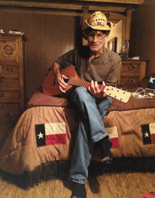 a man in a cowboy hat is playing a guitar on a bed with a texas flag on it