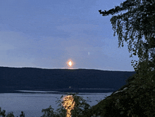 a full moon is visible over a lake with trees in the foreground