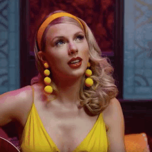 taylor swift is wearing a yellow dress and orange headband while playing a guitar .