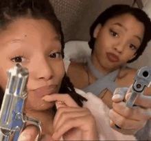 two young women are holding guns in their hands and taking a selfie .