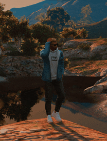 a man wearing a hoodie that says all stands on a rock near a body of water