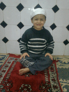 a young boy sits on a red rug with the word newy on his pants