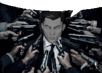 a man in a suit and tie is surrounded by lots of guns