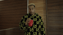 a man wearing a black and yellow gucci sweatshirt holds a red cup