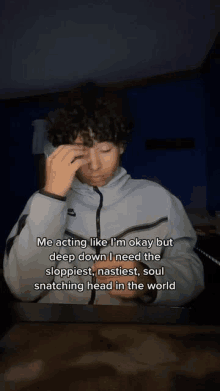 a young man with curly hair is sitting at a table with his hand on his forehead and a caption .