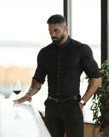 a man in a black shirt and black pants holds a glass of wine