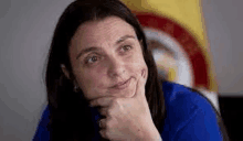 a woman with long hair is sitting in front of a flag with her hand on her chin .